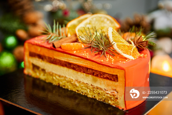 Christmas mousse apricot cutted cake with vanilla biscuit decorated with fruits on the background of candles, garlands, fir branches and cones