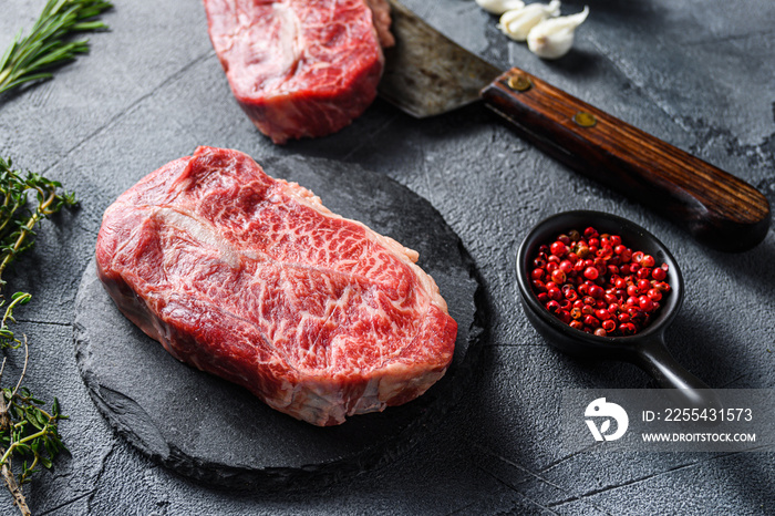 Raw top blade flat Ironcut, on black slate , and meat butcher cleaver marbled beef  with herbs tomatoes peppercorns over grey stone surface background side view close up