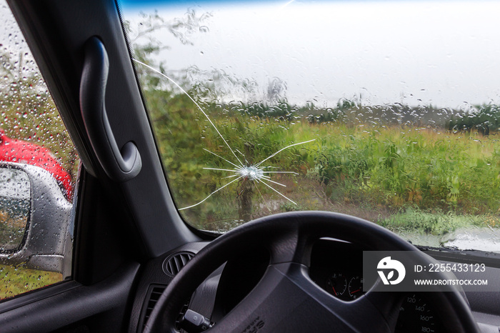 Broken windshield of a car. A web of radial splits, cracks on the triplex windshield. Broken car windshield, damaged glass with traces of oncoming stone on road or from bullet trace in car glass