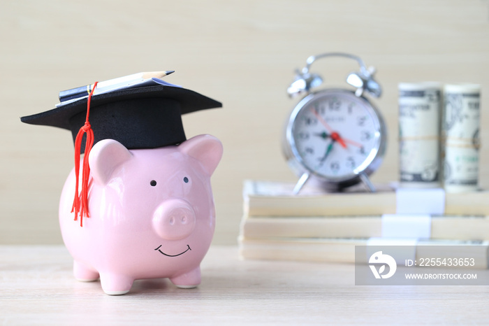 Graduation hat on blue piggy bank with stack of coins money on wooden background, Saving money for education concept