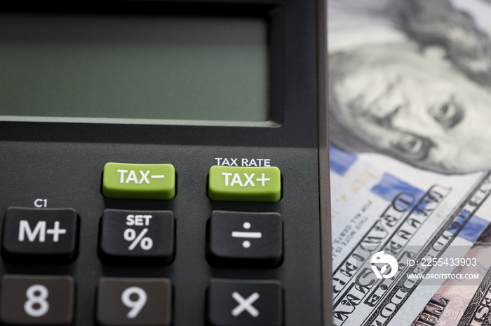 Tax cuts or reduce concept, Closed up shot of TAX minus / plus buttons with text TAX RATE on calculator with background of blurred US Dollar banknotes, United States government tax overhaul policy