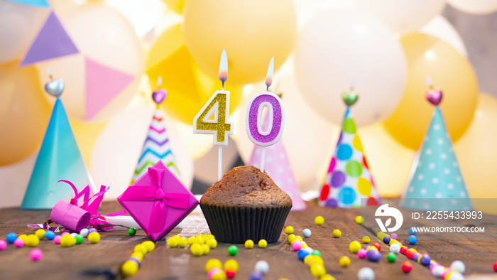 Happy birthday with a number of candles for forty years on the background of balloons. A festive muffin with burning candles and a pink gift box for a woman. Happy birthday for 40 years for a woman