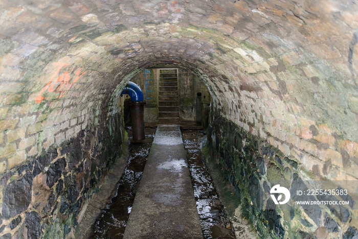 Dirty water runs down the sides of a path through a sewer tunnel