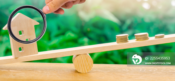 Wooden house with coins on the scales. The concept of real estate purchase. Sale of property. Payment of the mortgage. Redemption of taxes. Tax refund. Credit for the apartment.