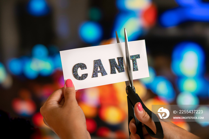 Woman hand are cutting over white paper with scissors over the word cant and converting it to the word can. City lights bokeh as background. Motivational and inspiraton concept.