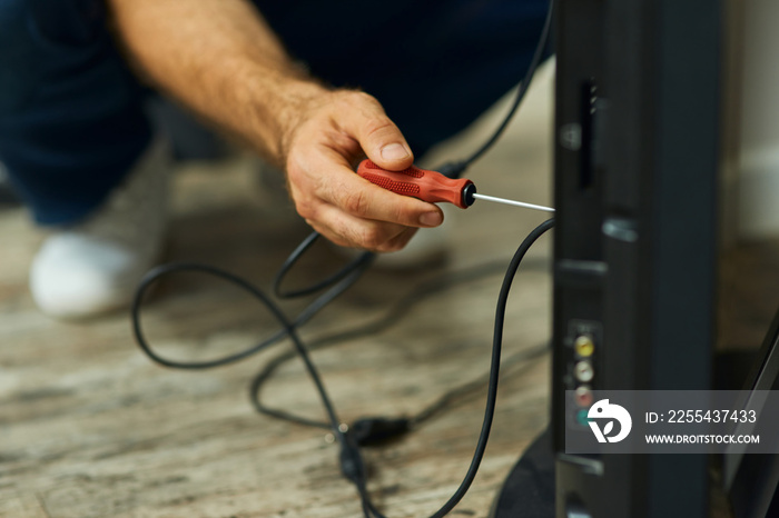 Handy home repair. Close up shot of hand of a repairman using a screwdriver while installing or fixing tv set indoors