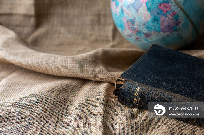 Close up of the old holy bible with blurred world globe on vintage linen sackcloth background against, copy space, Christian background, bible study or devotional concept.