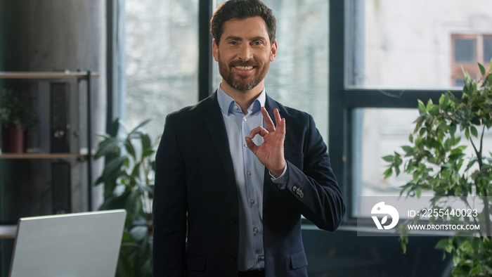 Smiling adult caucasian man in office look camera successful businessman professional manager entrepreneur showing ok sign approval gesture demonstrating support symbol excellent result recommendation