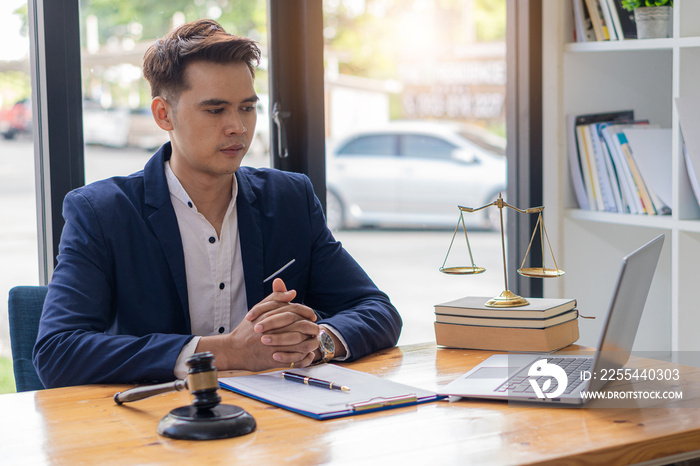 Asian male lawyer working on legal contract documents and hammer and scale with laptop placed in front in the courtroom. justice attorney and legal concepts