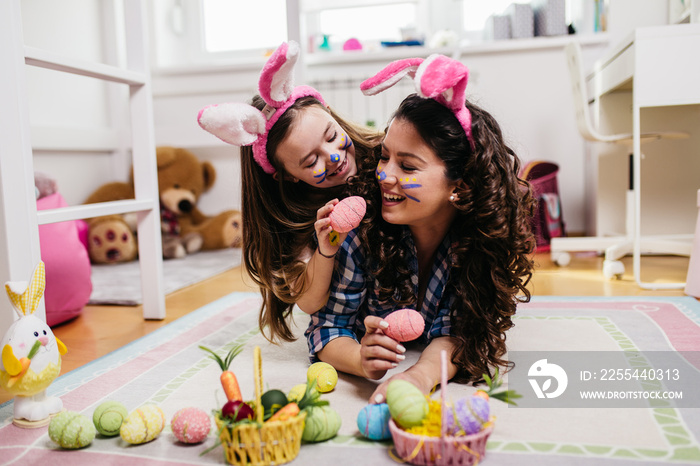 Mother and her cute little daughter playing in children’s room while preparing Easter decoration.