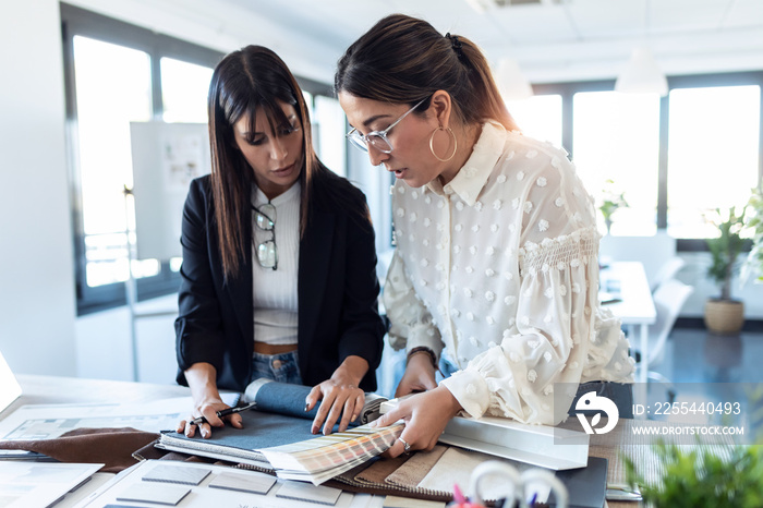 Two beautiful young designer women working in a design project while choosing materials in the office.