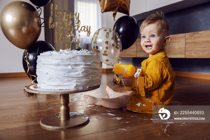 Cute little baby boy sitting on the floor, smashing and playing with his cake on his first birthday.