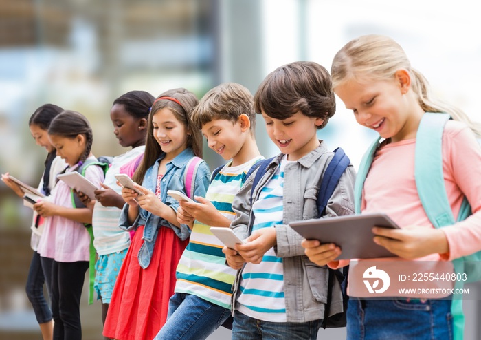 Group of diverse school students using electronic devices against blurred background