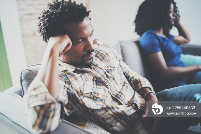 Young displeased black couple.Upset man being ignored by partner at home in the living room.American african men arguing with his stylish girlfriend,who is sitting on sofa couch next to him.Blurred