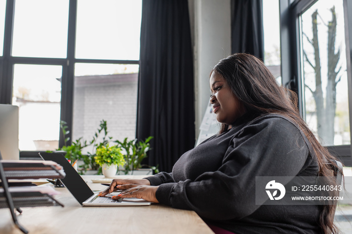 happy african american plus size woman typing on laptop keyboard in office.