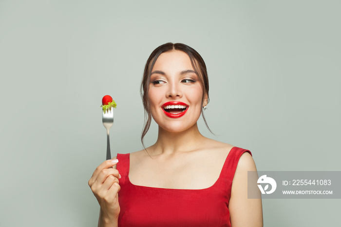 Beautiful happy woman holding fork with tomatoes and lettuce on white background