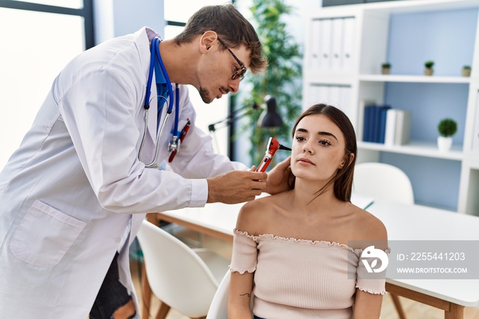 Man and woman wearing doctor uniform auscultating ear using otoscope at clinic