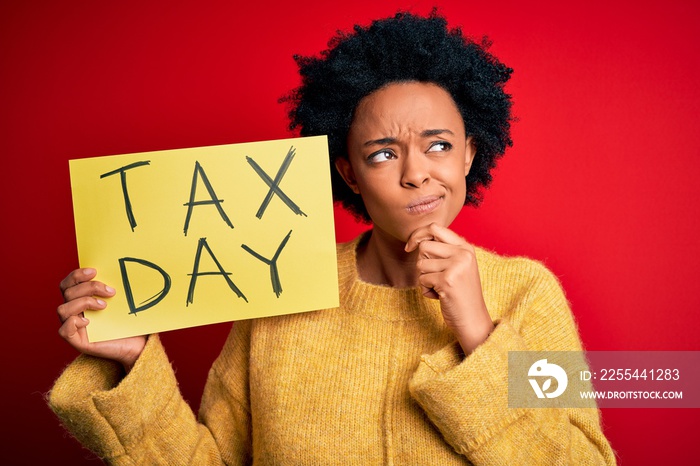 Young African American afro woman with curly hair holding paper with tax day message serious face thinking about question, very confused idea