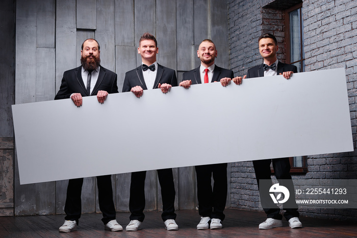 Your advertisement in good hands. Group of handsome young men in tuxedo holding big blank with copy space.