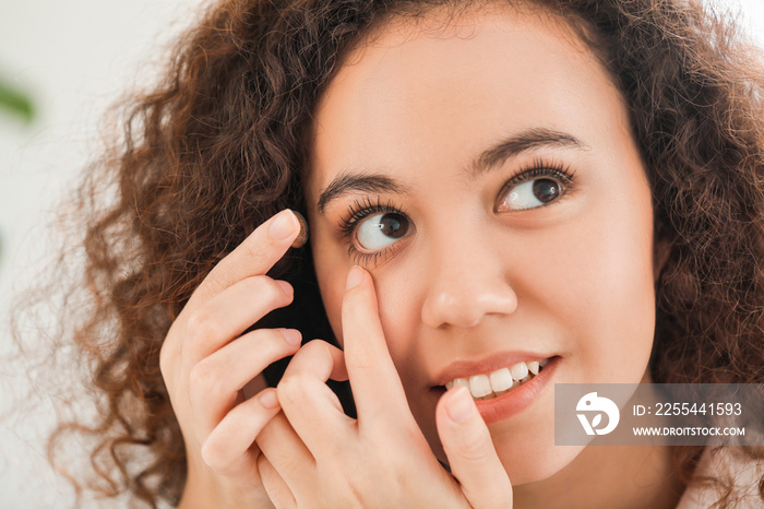 Young African-American woman putting in contact lenses at home