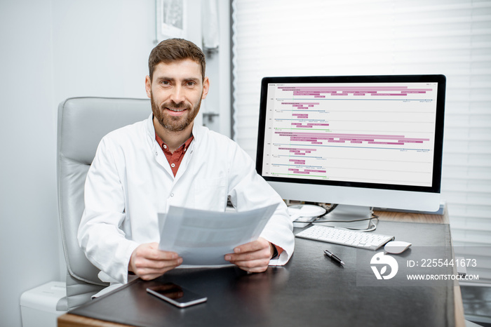 Portrait of a handsome doctor sitting in the luxury medical office with computer on the background