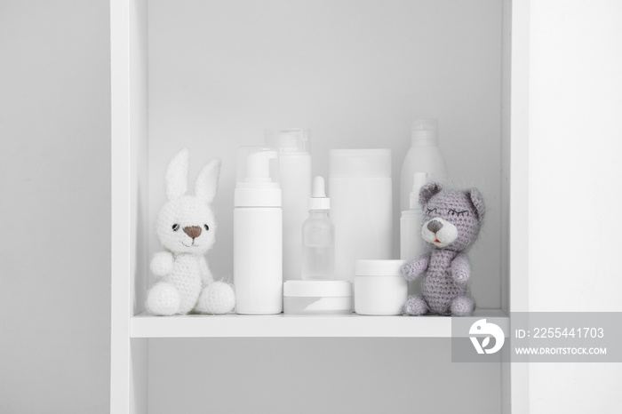 Cute knitted toys and bath accessories for children on shelf unit near white wall