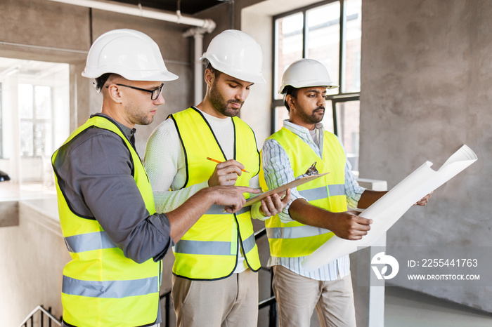 architecture, construction business and people concept - male architects in helmets with clipboard discussing blueprint in office building