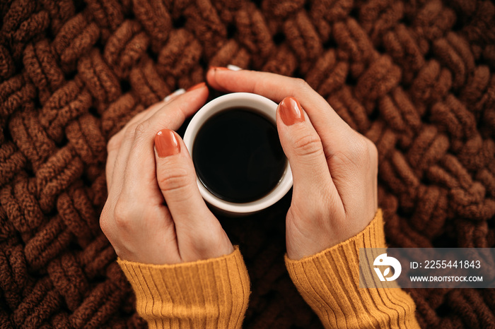 Women’s hands holding hot cappuccino coffee on the background of a knitted plaid. autumn vacation concept