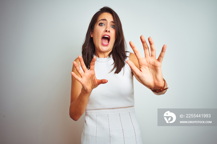 Young beautiful woman wearing dress standing over white isolated background afraid and terrified with fear expression stop gesture with hands, shouting in shock. Panic concept.