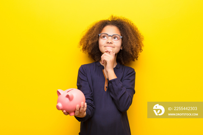 african american little girl  against flat wall holding a piggy bank