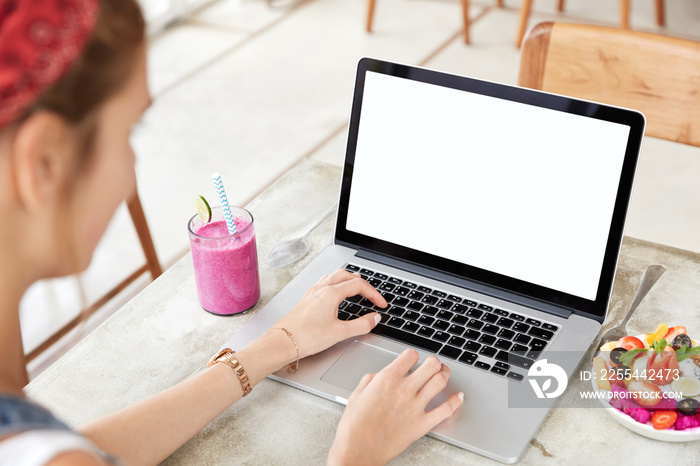 Successful businesswoman works distantly on modern generic laptop computer with blank screen for your promotional text, eats fruits and drinks tasty smoothie. Unreognizable female checks email