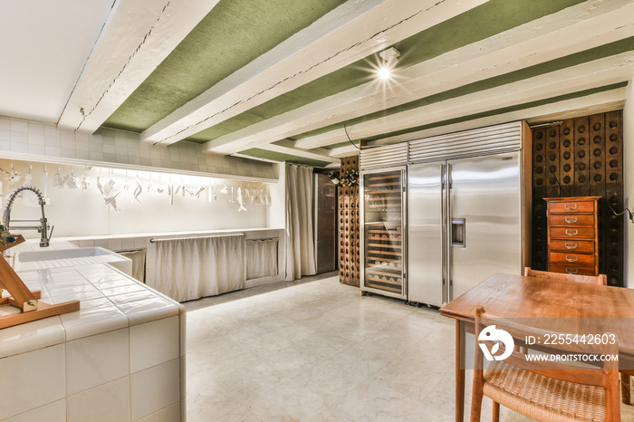 Contemporary big kitchen of mansion house with stainless fridge and wooden wine racks under white beams of ceiling