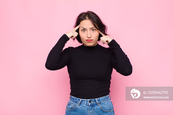 young pretty woman with a serious and concentrated look, brainstorming and thinking about a challenging problem against pink wall