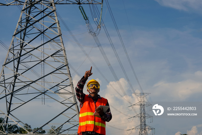 A male engineer uses a laptop and is inspecting the construction work. A large electric power pole in front of the construction site.