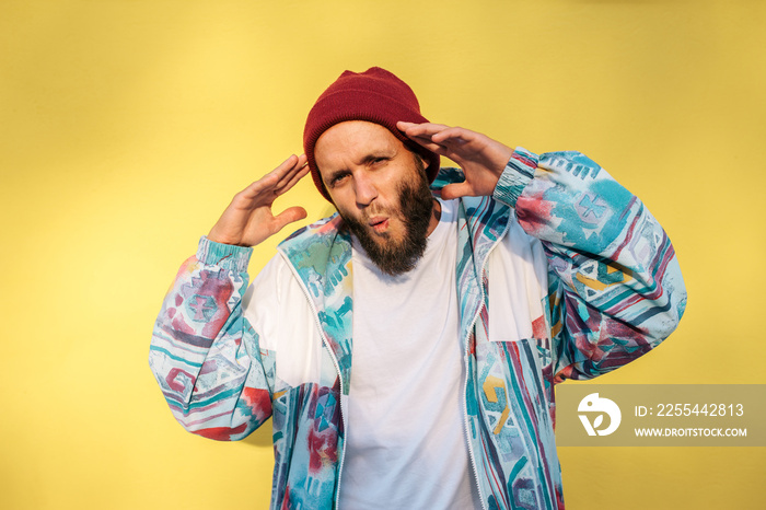 Stylish young hipster man with beard in red hat and a retro jacket of 90s on yellow background.Crazy hipster guy emotions. Collage in magazine style .