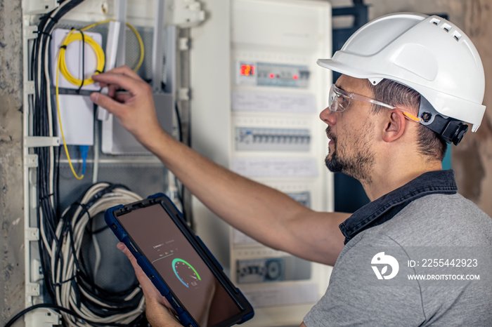 Man, an electrical technician working in a switchboard with fuses, uses a tablet.