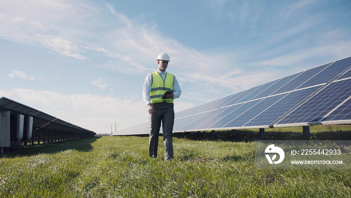 Professional worker walking along solar power station and using tablet.