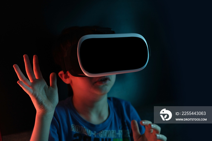 boy, child in dark room with neon lights in modern VR glasses interacting with network while having virtual reality experience, concept study of another world, modern teaching technologies