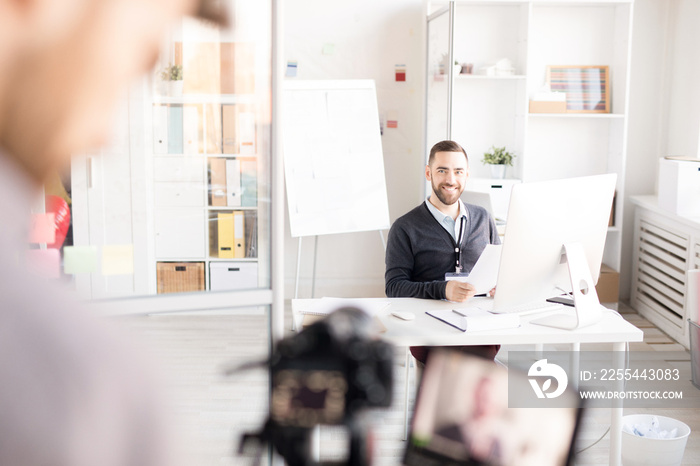 Portrait of smiling businessman looking at photographer while working at desk in modern office, copy space