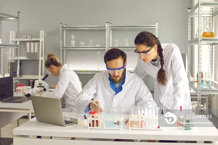 Team of young scientists working in modern laboratory. Pharma researchers or biotech science company employees in lab coats and goggles using special equipment and conducting scientific experiments