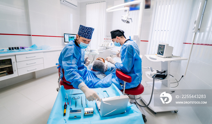 Dentists with protective mask and gloves repair tooth of young female client at modern ambulant.