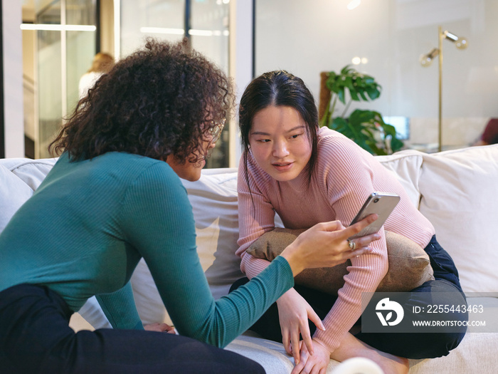 UK, London, Two female coworkers looking at smart phone in modern office lobby