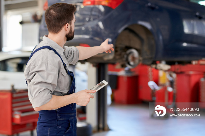 Back view portrait of modern bearded mechanic holding digital tablet pointing at car while working in car service and repair center, copy space