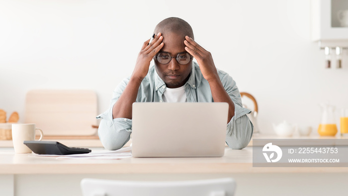 Expensive modern life. Disappointed mature african american man calculating taxes or planning budget, sitting in kitchen