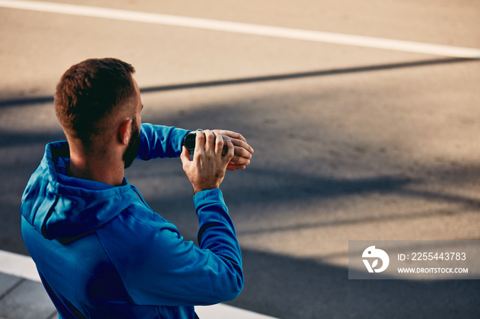 Runner setting smart watch while standing on the street. Healthy lifestyle concept. Backs turned.