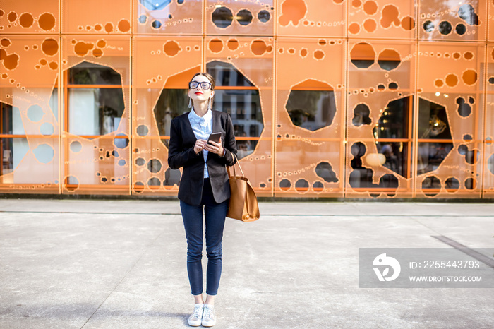 Portrait of a young businesswoman in the suit standing outdoors on the modern office wall background