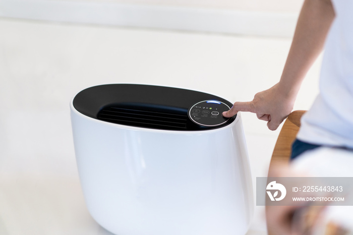 Asian woman relaxing in the living room while the modern portable air purifier working. Woman using air purifier in the living room to purify or clean the polluted air and atmosphere.