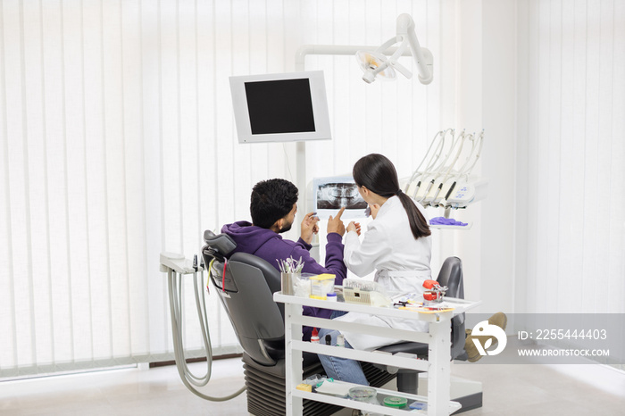 Medicine, dentistry and oral care concept. Female young asian dentist showing x ray picture to attractive patient, bearded man at modern light dental clinic.