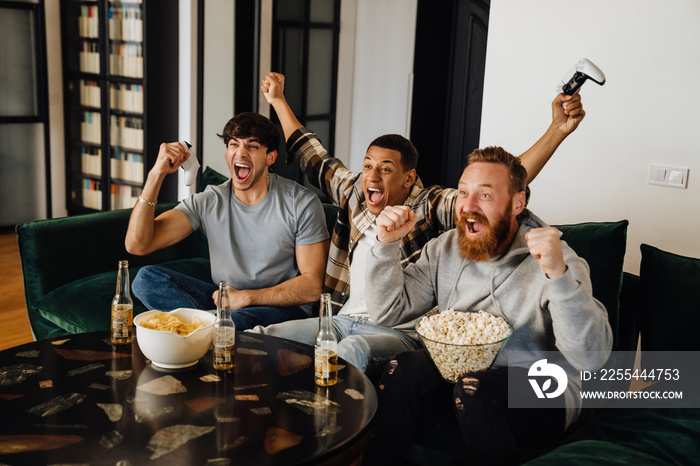 Three excited men gesturing as winners while playing video games at home