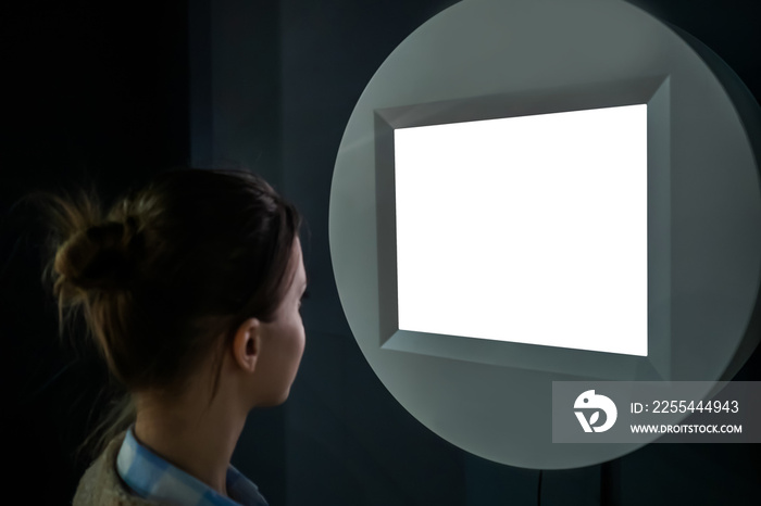 White screen, mockup, copyspace, template, technology concept. Woman looking at blank digital interactive white display wall kiosk at exhibition or museum with futuristic sci-fi interior